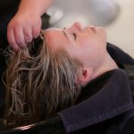 Mujer recibiendo un tratamiento de cabello en un salón de belleza, con estilista trabajando en su peinado